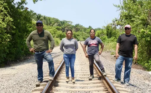 Four people stand on a train track.