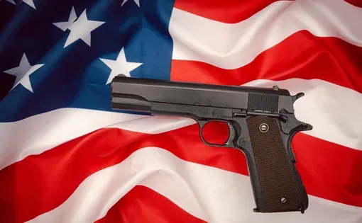 A handgun on the American flag background. Top view. Image by Meeboonstudio/Shutterstock.