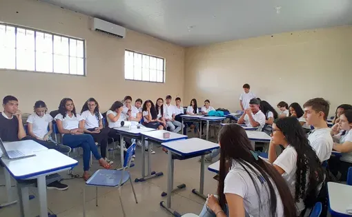 Students gather in a U-shape in a classroom to watch what projects from a laptop