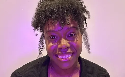 Shauntice, a Black woman with her curls in an up-do smiles at the camera