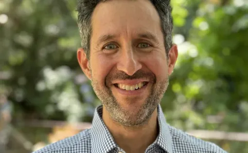 Headshot of man smiling in blue dress shirt with trees in background