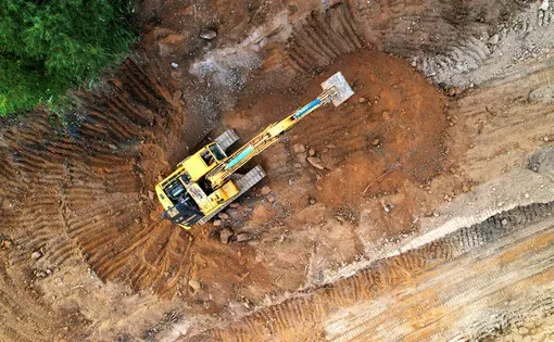 Excavator on earthmoving at construction site. Excavator on earthworks. Open pit development and sand mining. Loader digg ground, top view. Earthmover and digger on groundwork. Image by Maksim Safaniuk/Shutterstock.