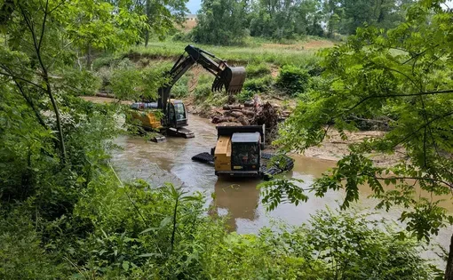 Equipment and logs are shown at a creek.