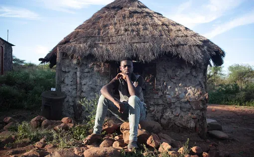 A young man sits outside a hut