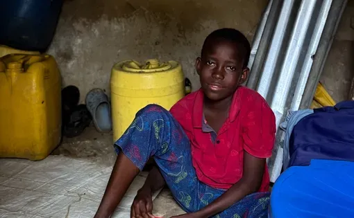 A boy sits on a floor wearing a red shirt and blue pants