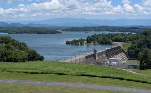 A dam holds back a large blue lake with green mountains in the background