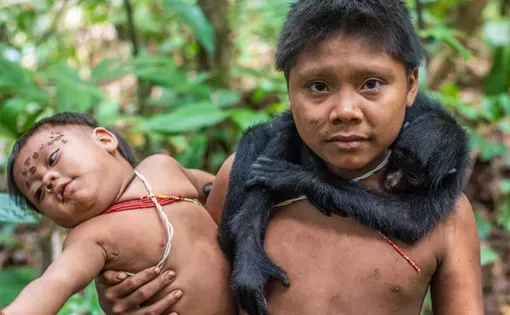 A child from the isolated Korubo community carries his brother and a pet spider monkey.