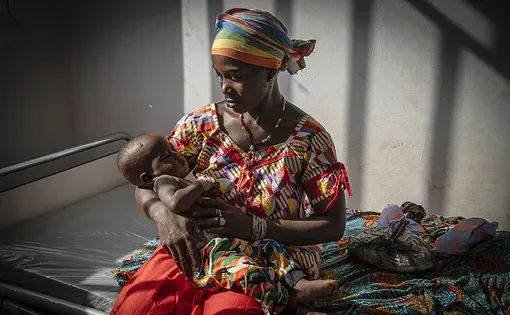 A mother sits on a bed holding her baby