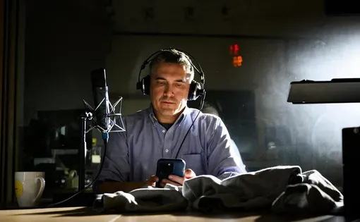 Man sits at radio desk looking at phone