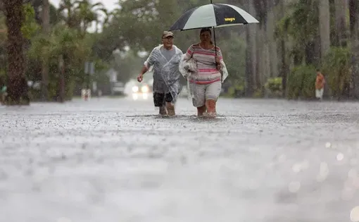 Two people walk on a flooded road as it rains.