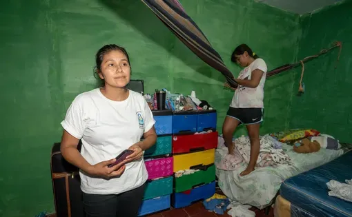 A woman in a white shirt stands in a room with green walls.