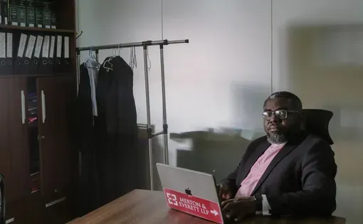 With a laptop in front of him, a man sits at a desk in an office