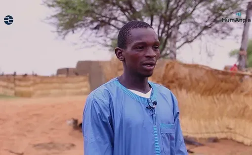 A man talks to the camera in front of a barren desert landscape