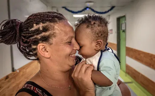 A woman smiles while holding a baby close to her face