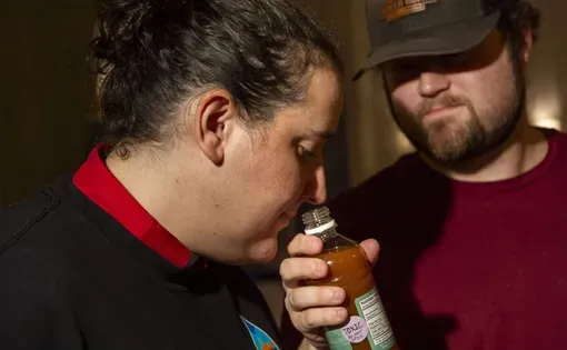 A woman smells water that's in a bottle being held by a man.