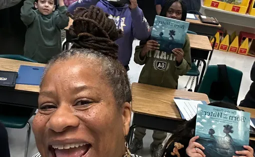 Project Lead, Veronica Jones, takes a selfie with students holding up copies of Born On The Water in the classroom