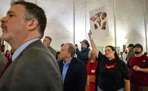 The Rev. Caitlin Ware hoists a sign reading “I thirst” at a news conference hosted by From Below: Rising Together for Coalfield Justice in the West Virginia Capitol Rotunda on Feb. 16, 2026.