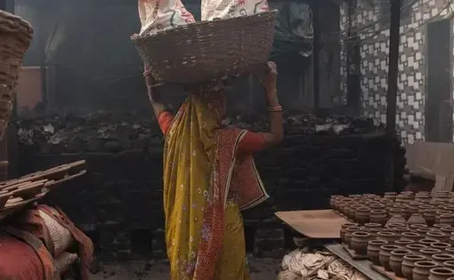 A potter woman carrying baked pots overhead from the lanes of her Kumbharwada to the main road, where they are stacked in tempos to be circulated across the city to traders and even outside. | Photo Credit: Godson Wilson
