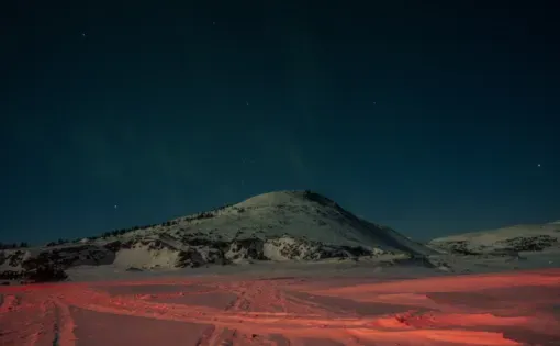 The aurora borealis can be seen in the clear winter sky and reflected as a scarlet glow on the ice on the outskirts of Nain, creating a colourful and surreal nightscape. Image by Johnny C.Y. Lam. Canada.