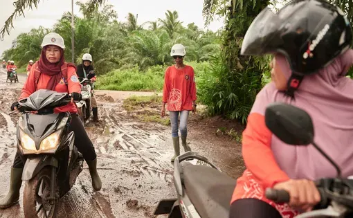 Women ride motorbikes in a forest.
