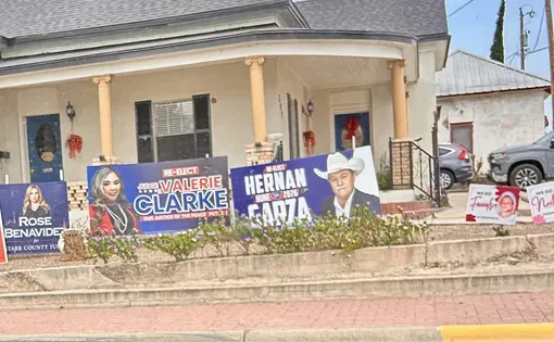 Campaign signs sit in front of a tan house.