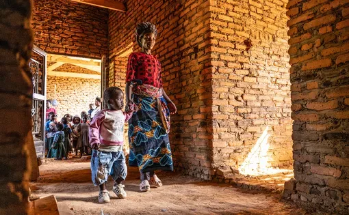 Joyce Chavula and her 3-year-old, Trust, walk through the unfinished health post at Katenje, in central Malawi