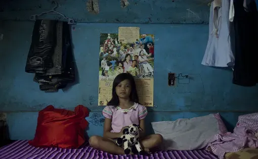 a young girl sits in front of a blue wall on her bed