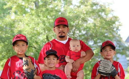 A man and his four children wear baseball uniforms.