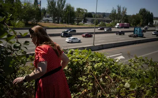 Livia Perkins walks through bushes on a freeway overpass.