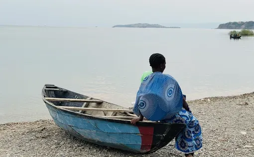 A woman fish trader waits for boats returning from a night of fishing at Ngwenya Landing Site in Mpulungu District, hoping to secure fish to sell. Image by Annie Zulu.