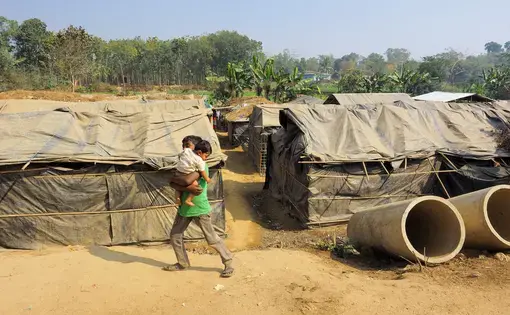 A boy carries another child in Kutapalong Refugee Camp. In this unofficial camp, tents are constructed with plastic tarps that had been used to evaporate seawater. Image by Doug Bock Clark. Bangladesh, 2017.