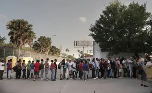 Migrants line up for food at a camp located on the Matamoros, Mexico, side of the Gateway International Bridge that connects Matamoros to Brownsville, Texas. Church and volunteer organizations in Brownsville provide water and food for the migrants on the Mexican side of the border as they wait for their asylum requests to be processed. Image by Jose A. Iglesias. Mexico, 2019.