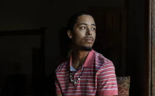 Gabriel Dickerson sits for a portrait wearing blue jeans and a T shirt.
