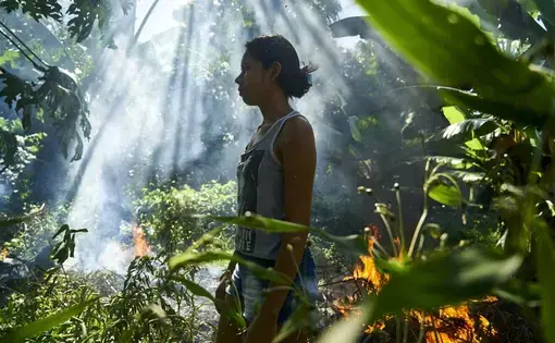 Joane beside a bonfire used to burn plastic waste. Image by Pablo Albarenga. Brazil, 2019.