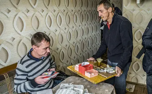 Vyacheslav Ignatenko (right), holding a tray of opiate cooking equipment, receives bags of syringes from a needle exchange in Kazan, Russia. Image by Misha Friedman. Russia, 2018.
