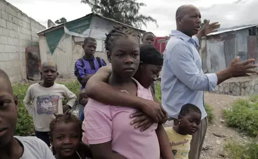 Cami Etienne, far right, talks about the situation in Haiti in the company of some of the children who live in a makeshift camp located off a dirt road in the interior of Delmas. Image by Jose A. Iglesias. Haiti, 2019.