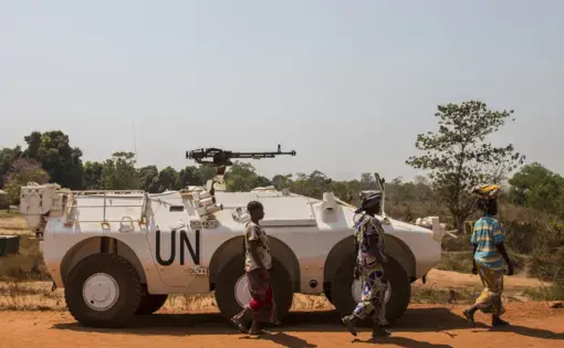 Women walk past a U.N. vehicle at the entrance to the sprawling camp in Kaga-Bandoro for thousands of families displaced by civil conflict. Image by Jack Losh. Central African Republic, 2018.