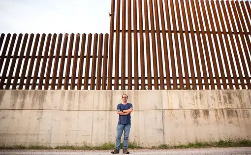 Scott Nicol, co-chair of the Sierra Club’s Borderlands Campaign, stands in front of a concrete levee topped by the border fence in Hidalgo County. Environmentalists, along with the U.S. Fish and Wildlife Service, say the barrier endangers wildlife because animals can't reach dry land during floods.  Image by Callie Richmond. United States, 2017.