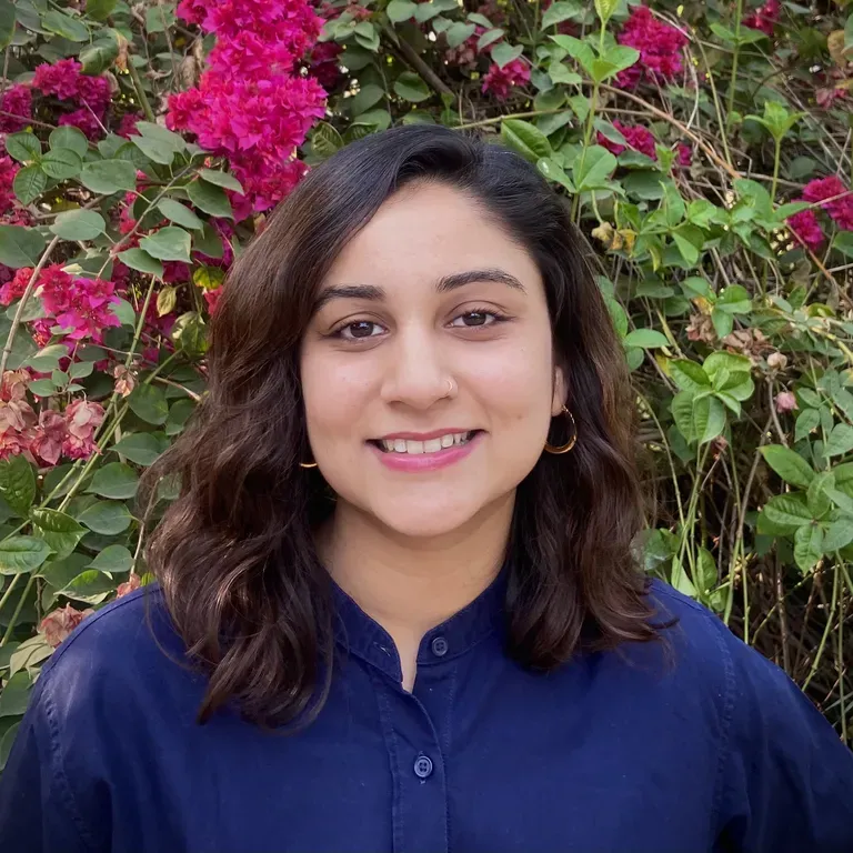Headshot of Sidrah Fatma Ahmed. She stands in front of a flowering bush.