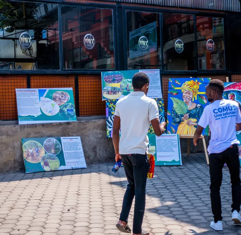 two people stand in front of a group of canvases in an exhibition