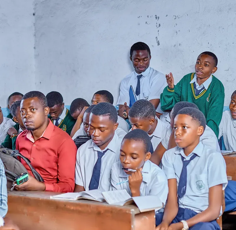 a group of schoolchildren sit in a classroom with the teacher speaking