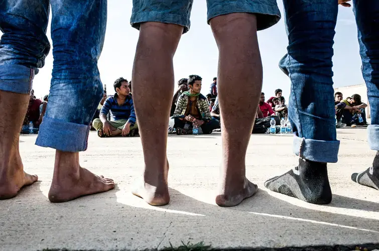 Migrants whose boat was intercepted by the Libyan navy wait to be given shoes before they can be moved to a detention center in Tripoli. Image by Peter Tinti. Libya, 2017.