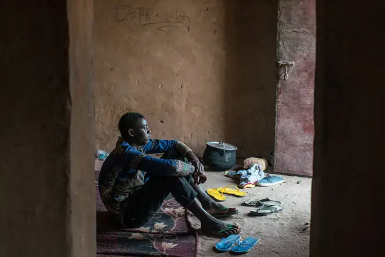 Sheriff Sonko sits inside the migrant ghetto in Agadez where he has been stranded for the last eight months. He left Gambia without telling his parents so they couldn’t try to talk him out of making the dangerous journey to Europe, but he ran out of money in Niger and is waiting for a family member to send more so that he can continue on to Libya. Image by Nichole Sobecki. Niger, 2017.