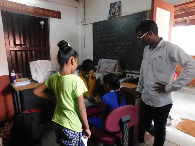 Manav Sadhna Health Coordinator Ajay Vaghela watches a nurse draw the blood of a local girl for testing at the Pediatric Camp. Image by Ambar Castillo. India, 2017.