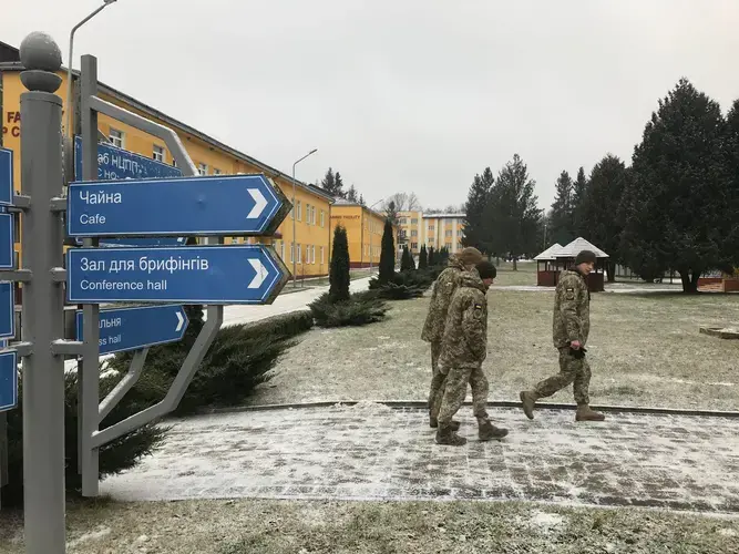 Ukrainian soldiers walk past a sign in English and Ukrainian on a combat training facility in western Ukraine. A Wisconsin National Guard unit arrived in November to mentor Ukrainian military trainers. Image by Meg Jones / Milwaukee Journal Sentinel. Ukraine, 2020.