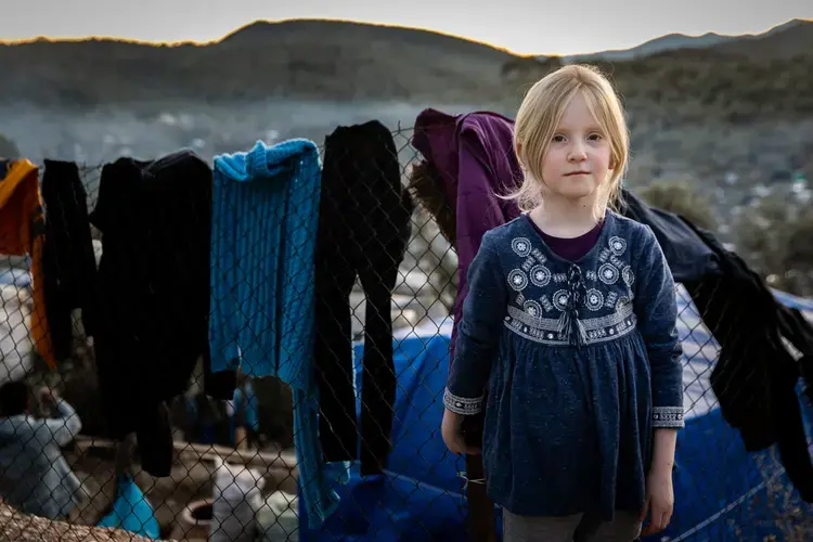 A young girl stands near the laundry she hung to dry in Moria on Lesbos on January 4, 2020. Approximately one-third of the over 20,000 people in Moria are children, and an estimated 1,500 of them are unaccompanied minors. Image by Maranie Staab. Greece, 2020.