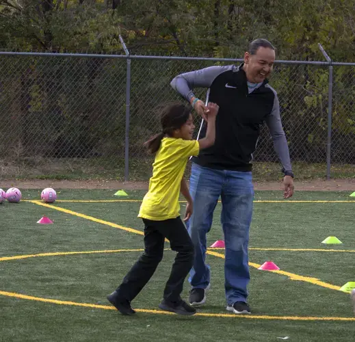 Justin Huenemann helps Lyonel up after a brief tumble on the soccer field. Throughout the clinic the students wore name tags. Huenemann explains that they like to call kids by their names. This makes for a more supporting and intimate interaction. Image by Viridiana Vidales Coyt. United States, 2017.