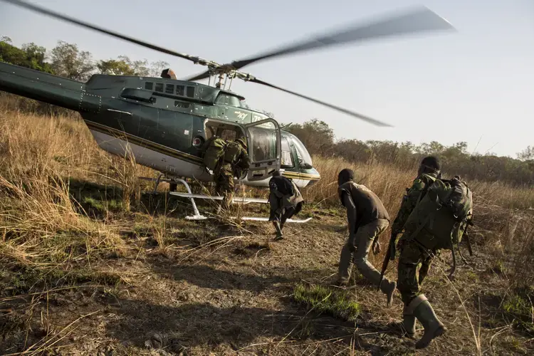 Rangers escort two poachers onto a helicopter after catching them hunting game in the Chinko wildlife reserve. Image by Jack Losh. Central African Republic, 2018.