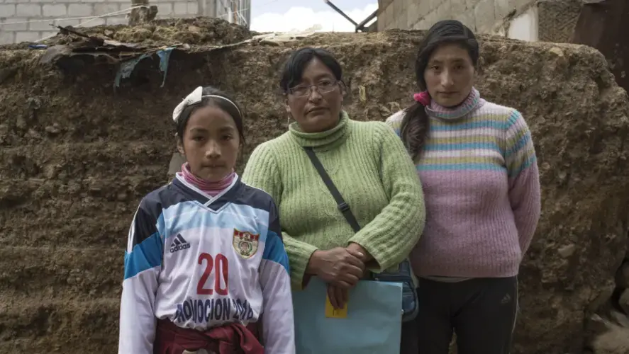 Sunmi (left) and Máyori (right) with their mother in their home. Sunmi was diagnosed by the Health Ministry in September 2015 with developmental disabilities, learning disability and chronic epistaxis (nosebleeds) from high levels of lead in her bloodstream. Image by Ricardo Martínez. Peru, 2017.