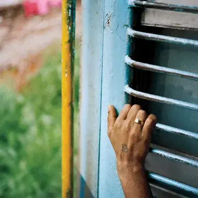 A passenger holds on to the open door as the train passes through Jammu. Image by Sara Hylton. Kashmir, 2017.<br />
